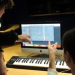 Music production students work collaboratively around computer display.