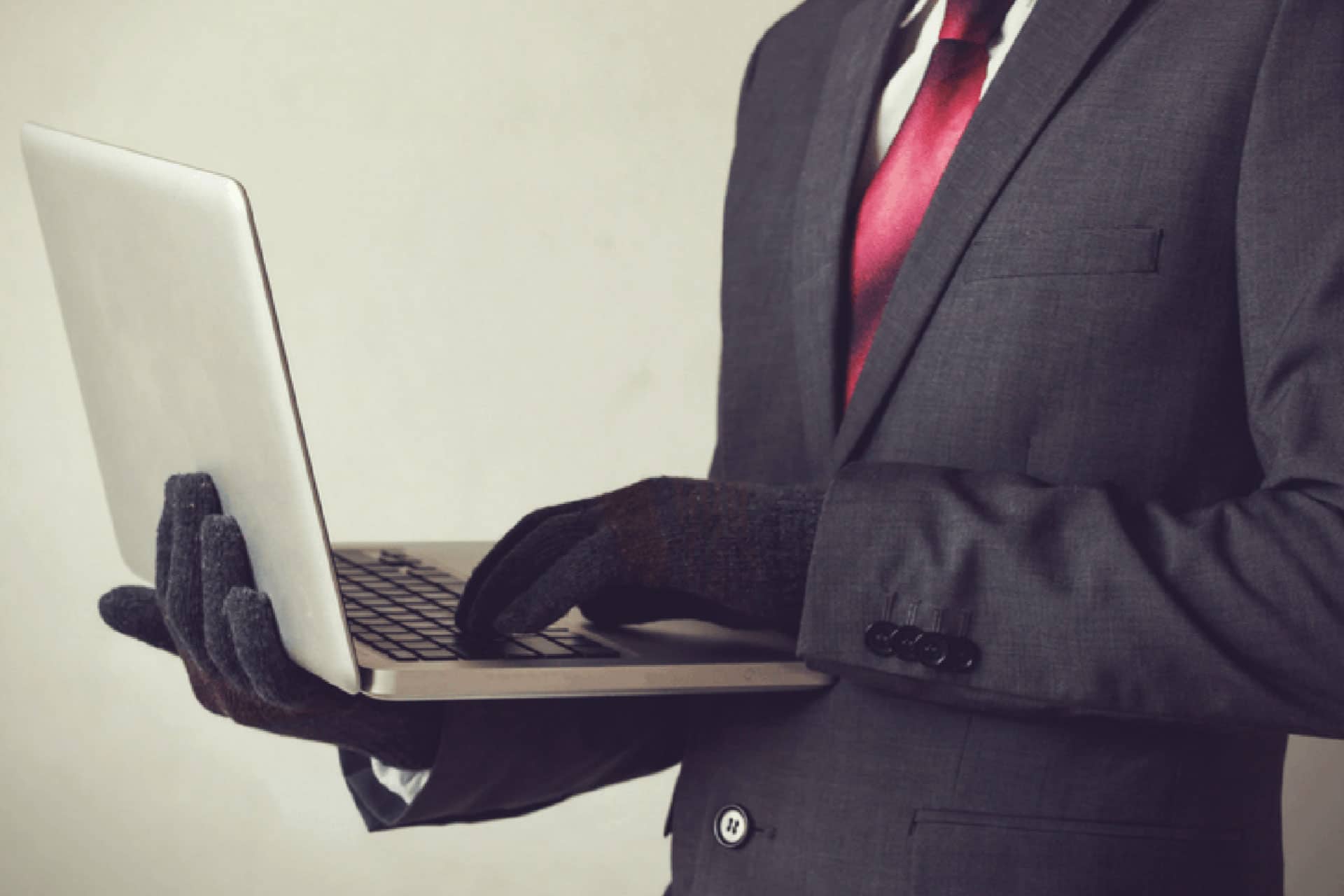 Suspicious main wearing a suit and gloves operates a laptop.