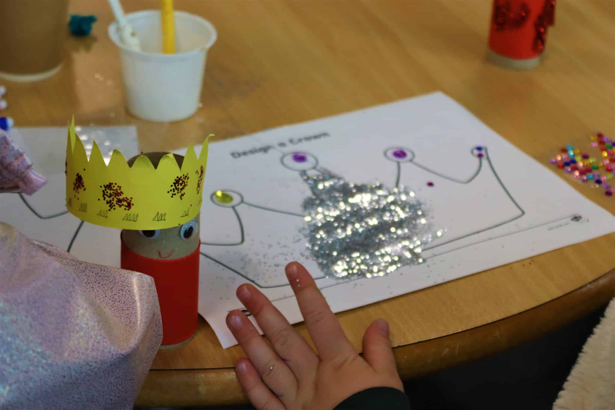 Person decorating and designing a paper crown next to a mini-king craft work at a coronation event with the local community