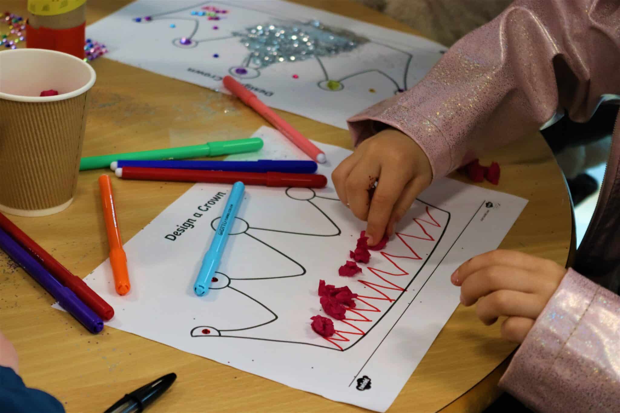 Person decorating and designing a paper crown at a coronation event with the local community