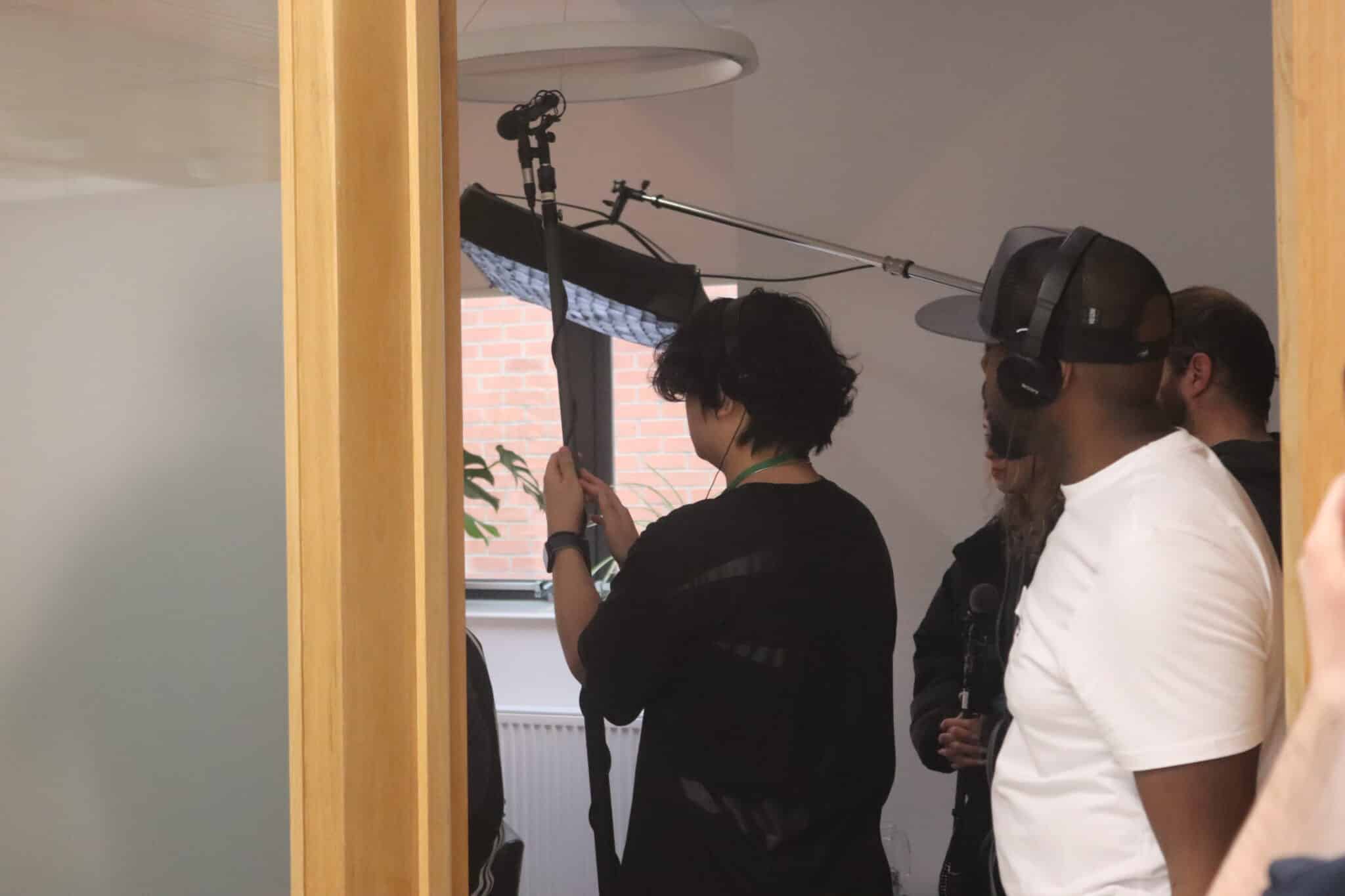 Sound crew with boom microphones in a room as college students work with BBC