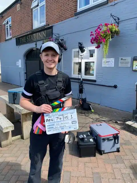 Man smiling on step holding a film clapper board