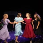 Students holding hands on stage in a dance sequence
