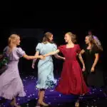 Students holding hands on stage in a dance sequence