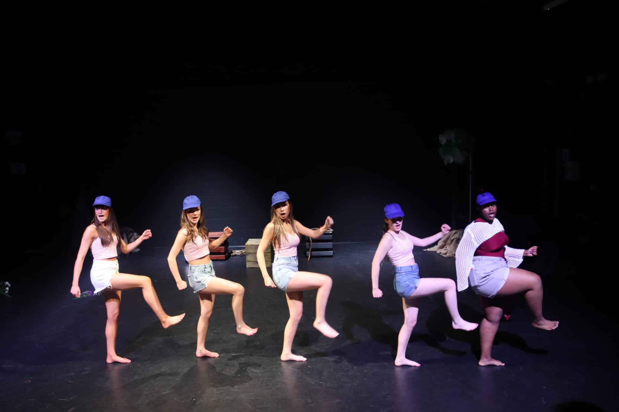 5 students wearing caps with their feet in the air dancing