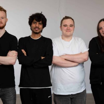 4 people stood in front of a blank wall smiling at the camera