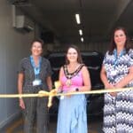 3 women stood by a golden ribbon cutting it.
