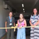 3 women stood by a golden ribbon cutting it.