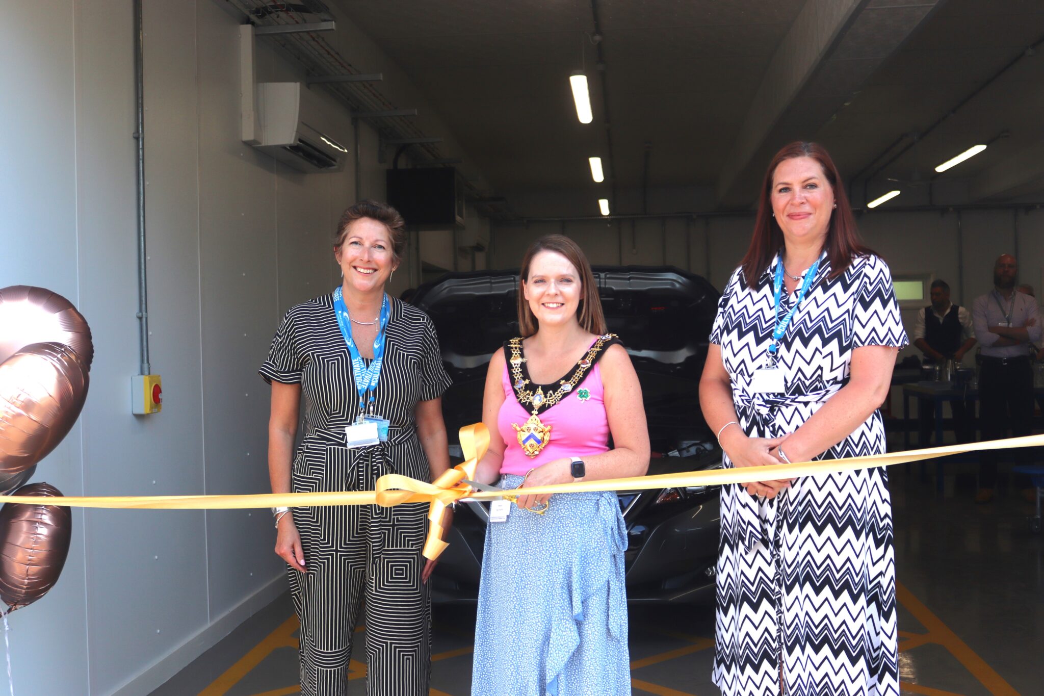 3 women stood by a golden ribbon cutting it.