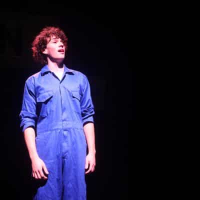 student singing in blue overalls