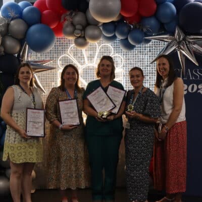 five people standing in front of balloons and lights with awards
