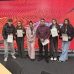 students and staff standing with certificates in front of red wall