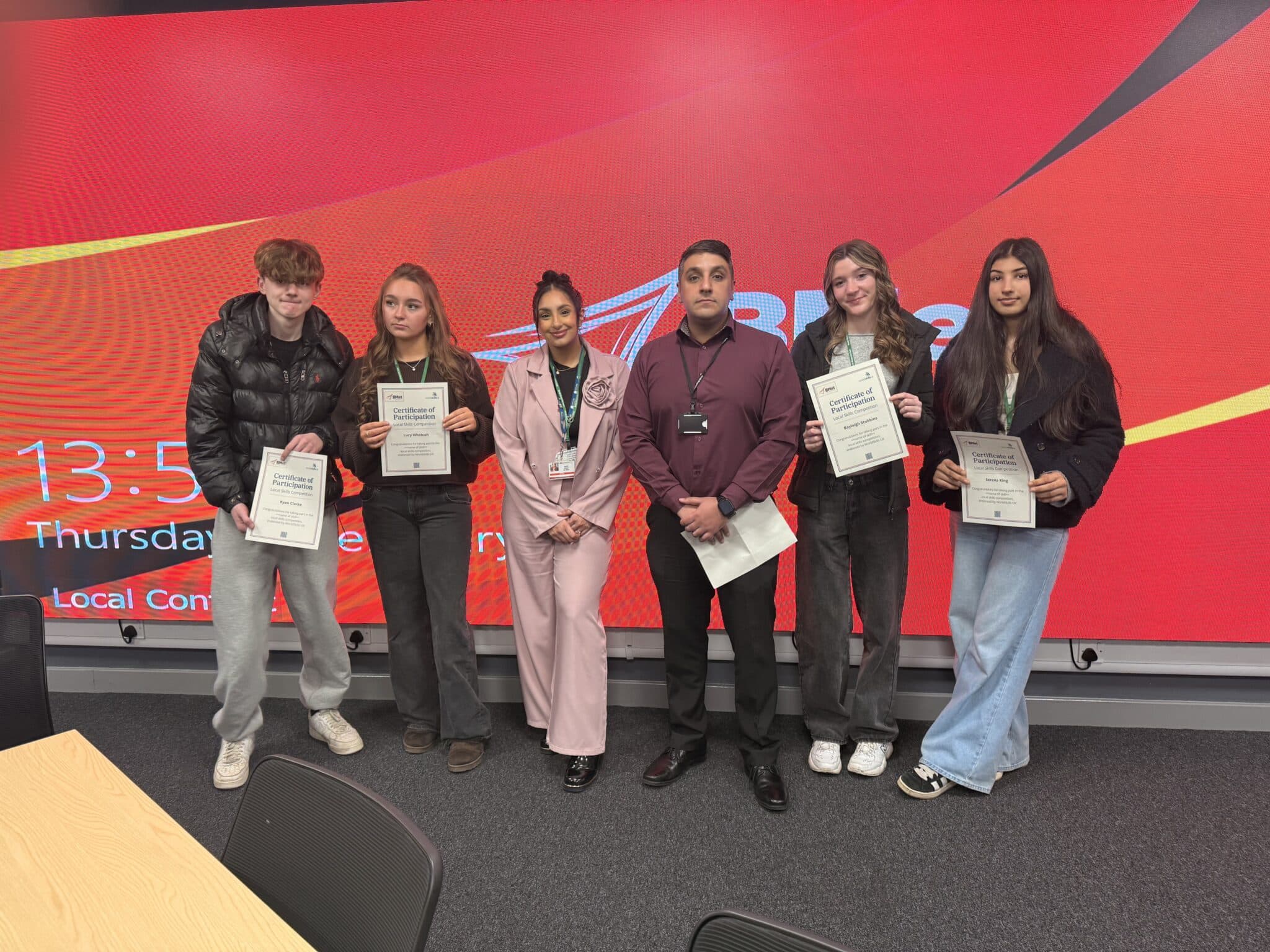 students and staff standing with certificates in front of red wall