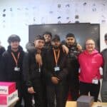 students standing with visitor in front of computer screen