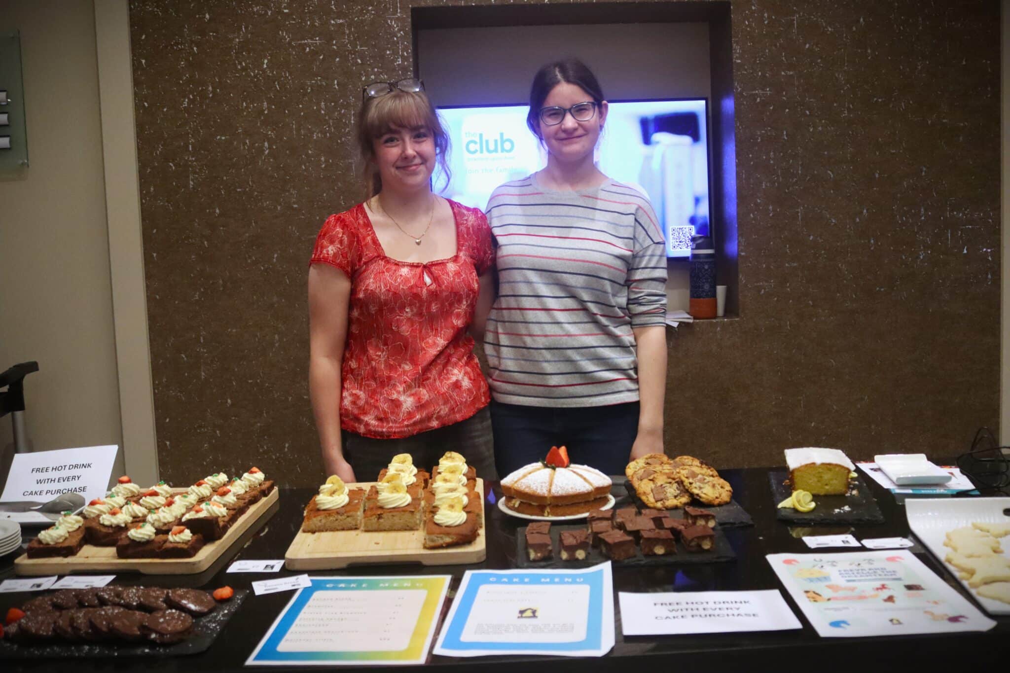 2 students stood behind a table of cakes