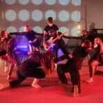 students playing guitar surrounded by dancers in black clothing