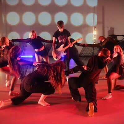 students playing guitar surrounded by dancers in black clothing