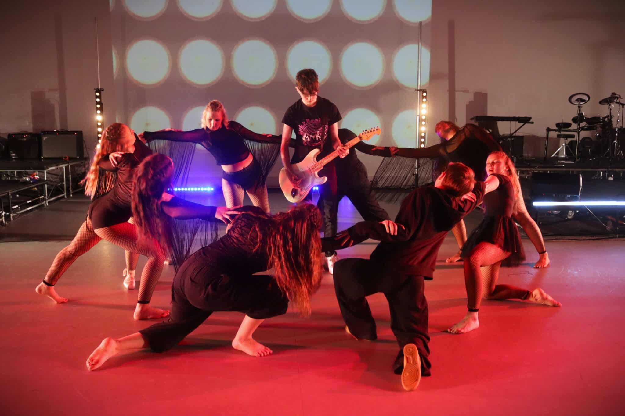 students playing guitar surrounded by dancers in black clothing