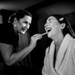 2 woman with one dressed in black the other in white doing make up