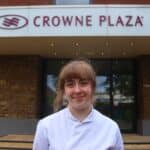 person in white uniform standing in front of a sign saying crowne plaza