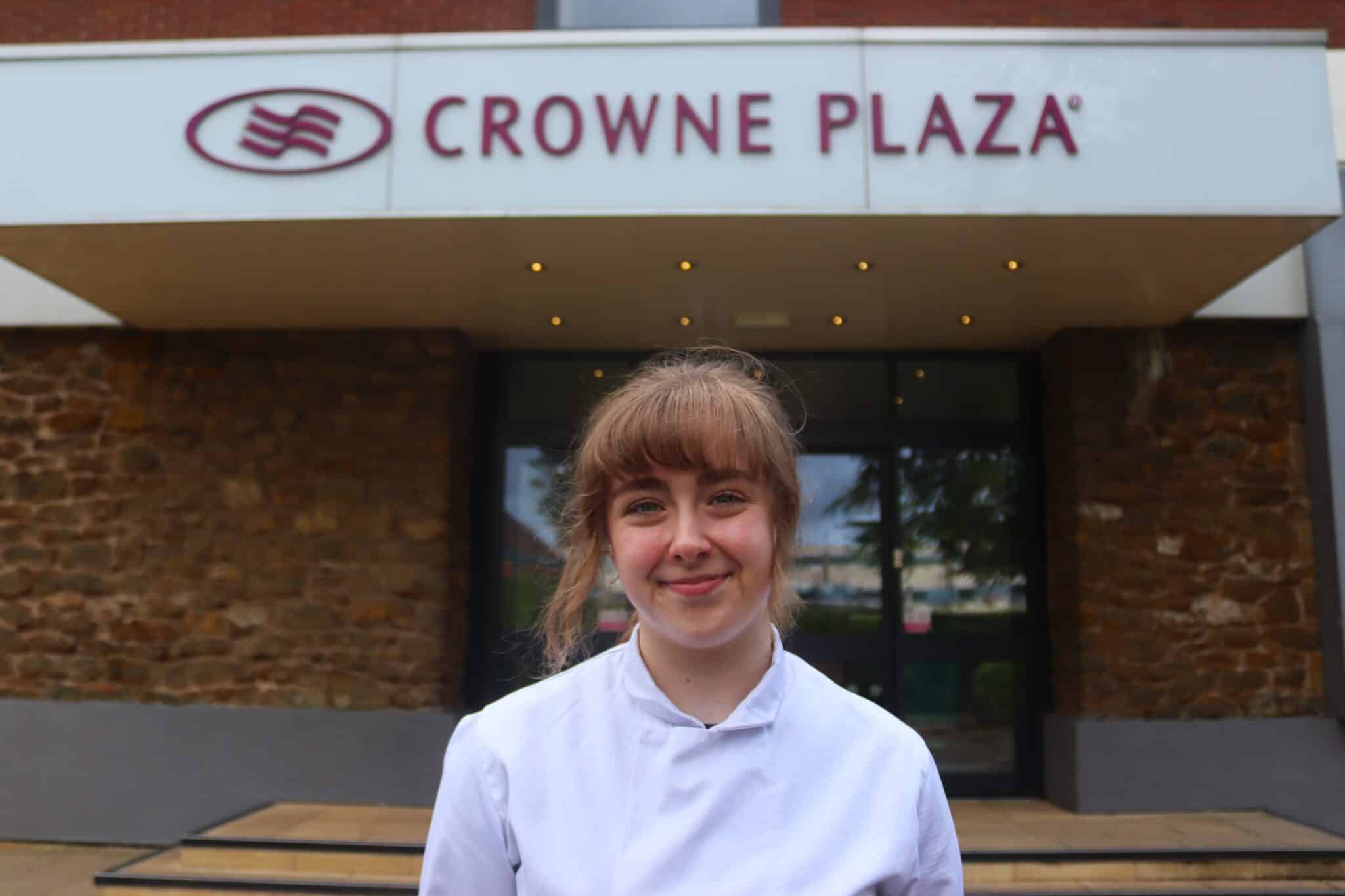 person in white uniform standing in front of a sign saying crowne plaza
