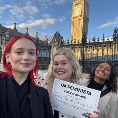 3 people standing in front of grand building holding a certificate