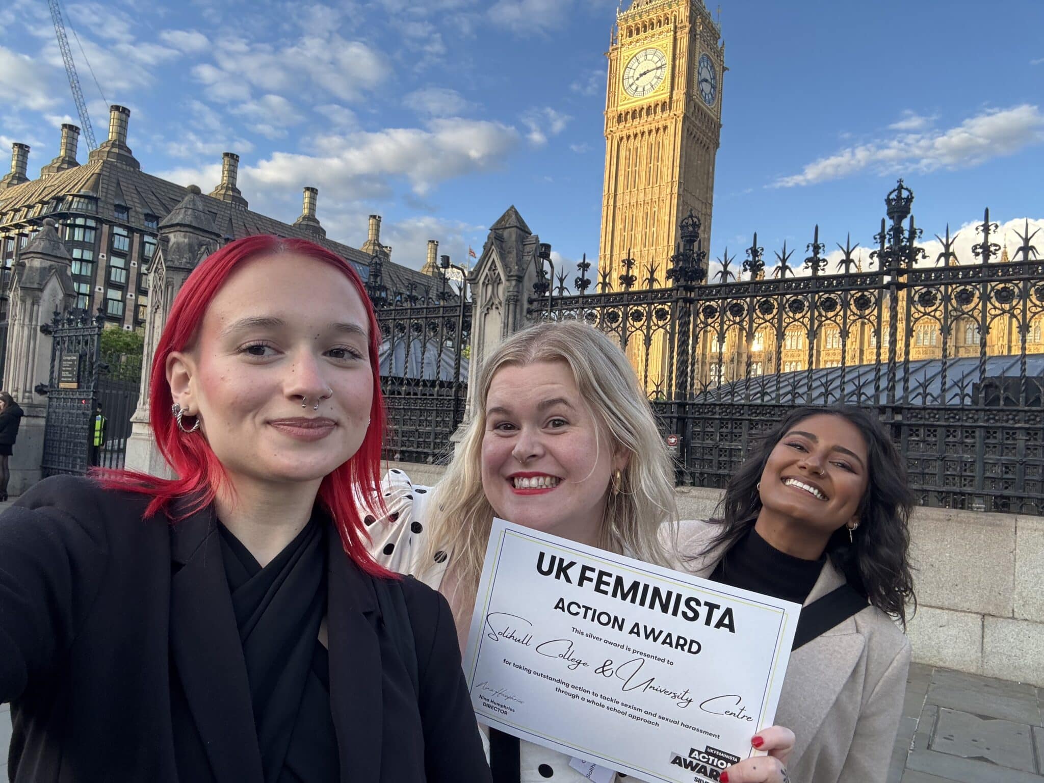 3 people standing in front of grand building holding a certificate