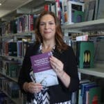 person stood in front of bookshelves holding book