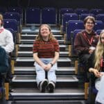 person sitting on stairs with students on chairs at edges of frame