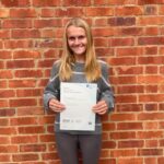 student in front of brick wall holding a certificate