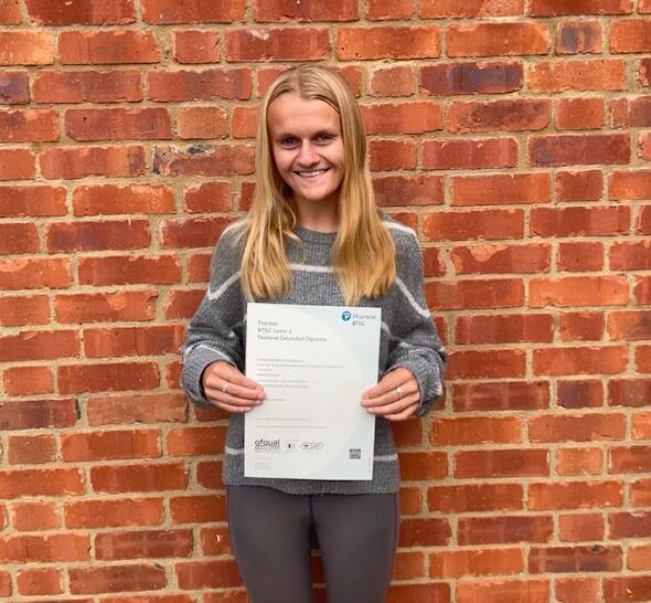 student in front of brick wall holding a certificate