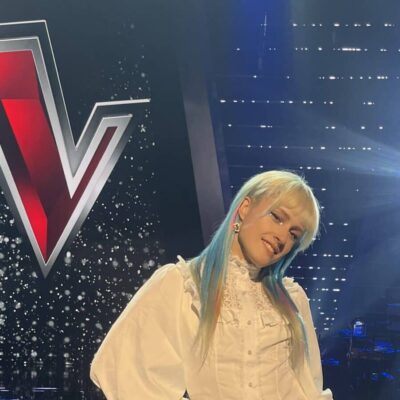 person stood on a stage in front of logo for the voice (a large red V)