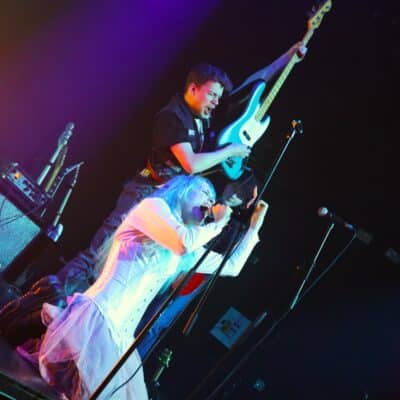 stundernt singing into a microphone knelt on stage with guitar player in background